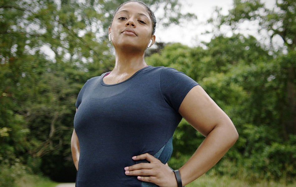 A centered view of a confident looking woman standing in front of a forest.